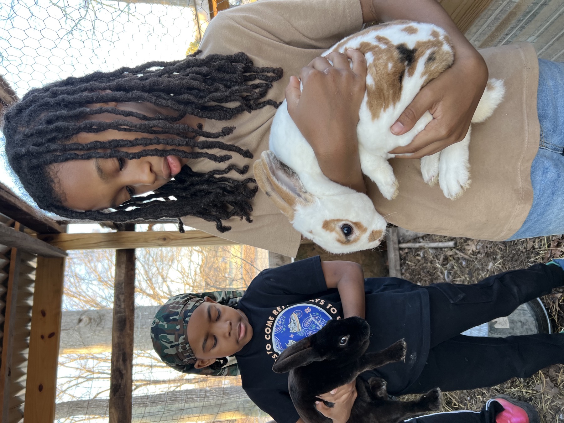 Two young growers holding rabbits in the Oasis Youth Farm hutch